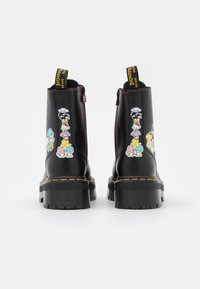 Botas de tobillo de charol negro con gráficos de personajes de dibujos animados coloridos, costuras rosas, una suela gruesa y tiradores decorativos.