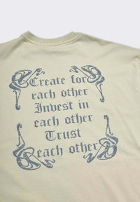 Tessuto beige con un testo gotico blu in stile invecchiato che recita "Crea per gli altri, Investi negli altri, Fidati degli altri", circondato da ornamenti decorativi.