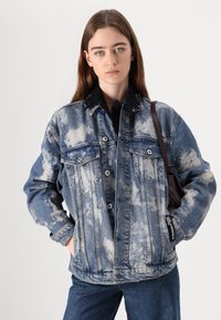 Denimjakke med en lys blå vask og blekede sky mønstre, to frontlommer og knapplukking. Svart skjorte med krage under.
