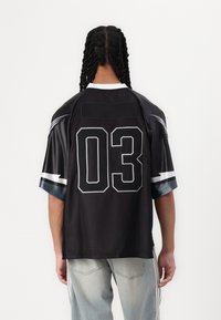 Un maillot de sport noir avec des manches courtes, un col ras du cou et un grand numéro blanc "03" imprimé au dos. Accentué de rayures grises.