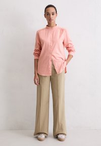 Light pink button-up shirt with a mandarin collar, long sleeves. Paired with wide-legged beige trousers and platform sneakers.