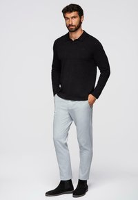 Polo a maniche lunghe nero, pantaloni grigi chiari e stivali Chelsea neri, con un design aderente e una texture liscia.