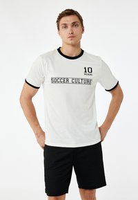 Biała koszulka T-shirt z czarnymi akcentami, z nadrukami "SOCCER CULTURE" i "10 MIAMI". W połączeniu z czarnymi szortami. Gładka tekstura.