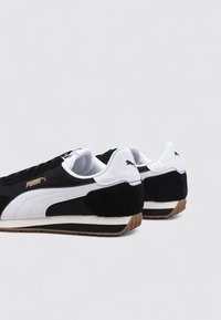 Czarno-białe trampki z zamszu i materiałów syntetycznych. Posiadają gumową podeszwę, ikoniczne logo Pumy oraz smukły, niskoprofilowy design.