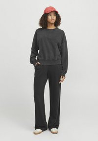 Schwarzer Sweatshirt mit einem cropped Design und lockerer Passform, kombiniert mit schwarzen weit geschnittenen Hosen. Das Model trägt eine rote Mütze und beigefarbene Turnschuhe.