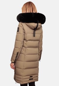Manteau d'hiver long beige matelassé avec une capuche en fausse fourrure noire, des zips sur les côtés et une étiquette en tissu au dos. Présente une texture matelassée et un design épuré.