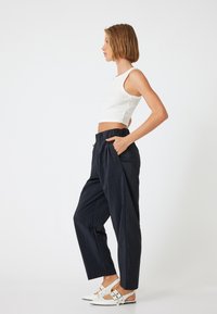 Lichte zwarte broek met een elastische tailleband en textuurstof, gecombineerd met een aansluitend wit geribbeld crop top en witte sandaaltjes.