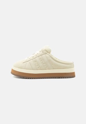 Beżowe buty sportowe na wsuwkę z wiązaniem z przodu, cholewką zamszową, potrójnymi paskami po bokach i grubą dwukolorową podeszwą w białym i brązowym kolorze.