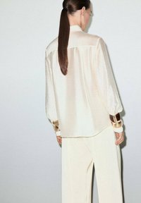 Cream blouse with a smooth texture, long puffed sleeves, and subtle polka dot pattern. Accessories include large bangle cuffs in varying colors.