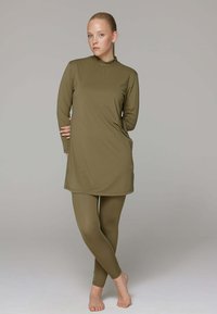 Olijfgroen sportset bestaande uit een langlevende tuniek-top en bijpassende leggings, gemaakt van een gladde, rekbare stof.