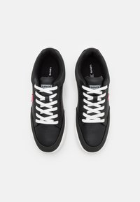 Baskets en cuir noir avec lacets blancs, bout rond et détails perforés. Présente un logo rouge Levi's sur le côté et une semelle intérieure rembourrée.