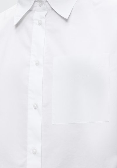 Chemise blanche à boutons avec col et poche poitrine présentant un texte brodé discret.