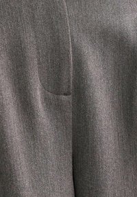 Tessuto grigio che mostra una texture liscia con una leggera lucentezza, caratterizzato da un dettaglio della tasca a toppa visibile sul lato sinistro.