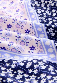 Mintás szövet virágos és geometriai mintákkal kék, orgona és rózsaszín árnyalatokban. Simább textúra, összehajtva, bemutatva a részletes kidolgozást.