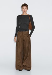 Pruhované černobílé tričko s dlouhým rukávem, doplněné hnědými kalhotami s vysokým pasem a širokými nohavicemi. Hnědá kabelka na rameno jako módní doplněk.