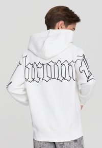 Biała bluza z kapturem z dużym czarnym napisem w stylu gotyckim "chrom" z tyłu. Posiada regulowany kaptur oraz ściągacze na rękawach i u dołu.
