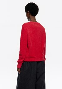 Suéter fuzzy rojo con cuello redondo y mangas largas, combinado con pantalones de pernera ancha en gris oscuro. Textura suave y corte relajado.