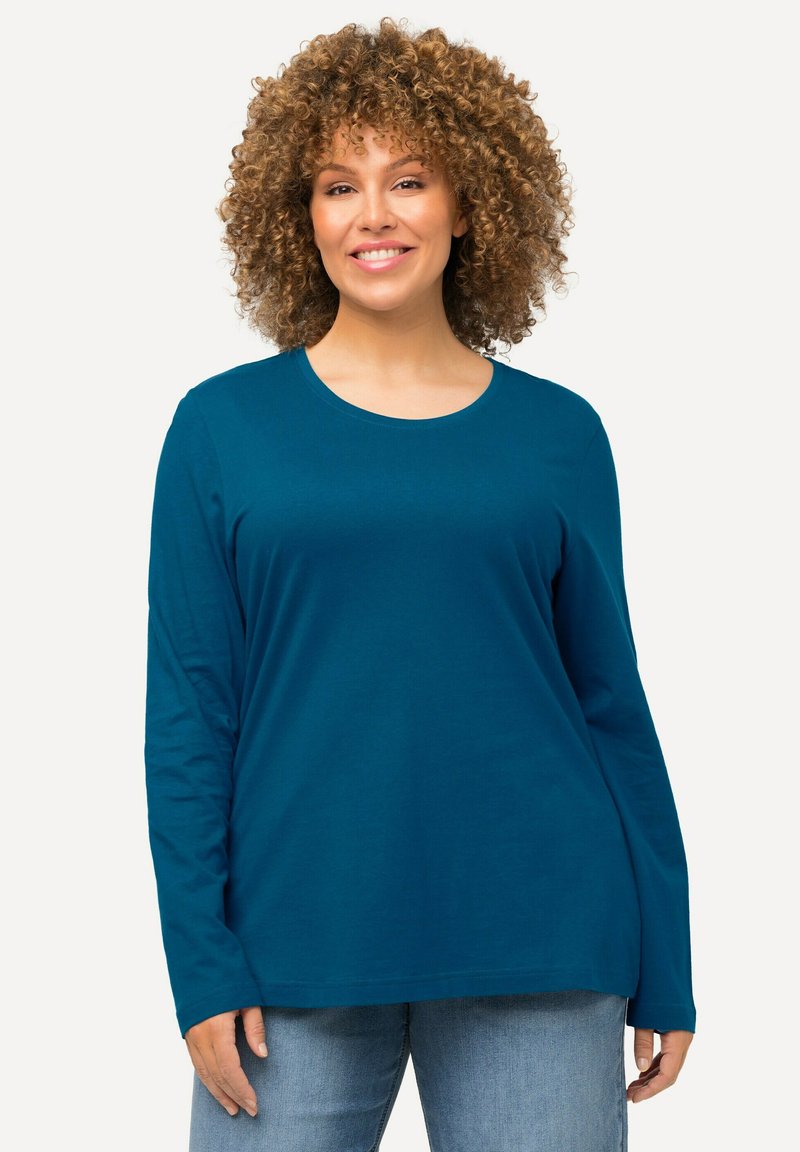 Langärmliges T-Shirt in Türkis mit rundem Halsausschnitt, aus weichem Stoff gefertigt, mit lockerer Passform und geradem Saum, kombiniert mit hellblauen Jeans.