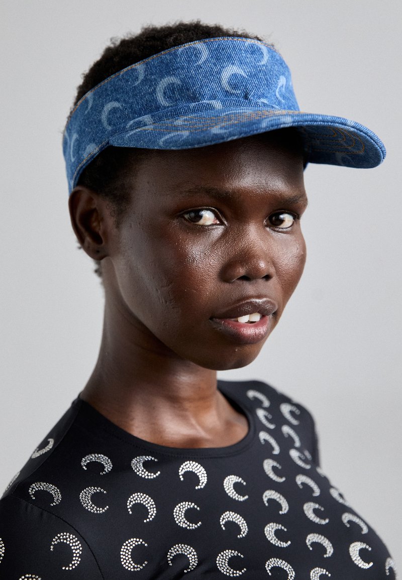 Blue denim visor with a patterned design, paired with a black top featuring silver accent details. Focus on texture and color contrast.