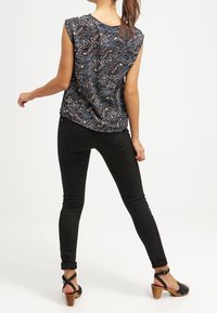 Černá bez rukávů blůza s texturovaným vzorem, zkombinovaná s úzkými černými džínami a černými sandály na podpatku. Pořízeno zezadu.