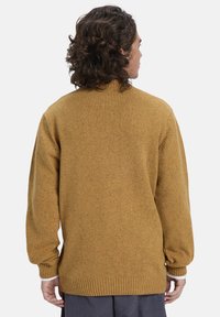 Bruine gebreide trui met geribbelde zoom en manchetten, met een ontspannen pasvorm en een textuur met gespikkeld stofdetail op het oppervlak.