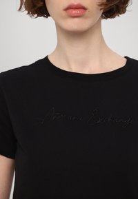 Černé bavlněné tričko s kulatým výstřihem a jemným vyšitým logem "Armani Exchange" na přední straně. Hladká textura.
