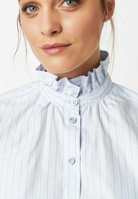 Light blue button-up shirt with vertical white stripes, ruffled high collar, and two light blue buttons at the front. Smooth fabric texture.