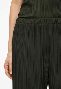 Grön plisserad jumpsuit i tyg med elastisk midja, som visar en vertikal ribbad textur och en slim fit.