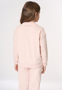 Felpa rosa chiaro con scollo rotondo a coste, spalle scese e maniche con polsini. Logo ricamato sul retro, abbinata a pantaloni coordinati.