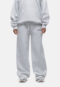 Grijze sweatshirt met een losse pasvorm en oversized mouwen, gecombineerd met bijpassende wijde sweatpants. Beide hebben een zachte textuur en minimale logo-details.