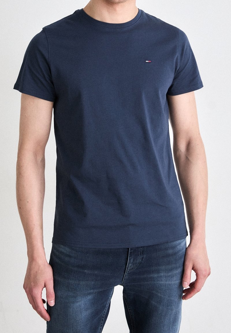Camiseta de algodón azul marino con cuello redondo, mangas cortas y un pequeño logo bordado en el lado izquierdo del pecho. Textura suave.