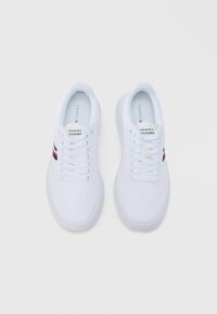 Beli superge z teksturirano platneno zgornjo plastjo, okrogel prst, ravne vezalke ter rdeče in mornarsko modre črte na straneh. Imajo oblazinjen ovratnik in logotip.