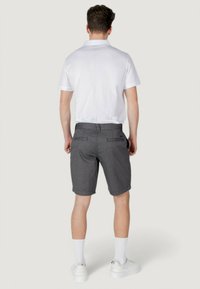 Maglietta polo bianca, pantaloni corti grigi a fantasia e sneakers bianchi. Tasche posteriori visibili sui pantaloni corti. Outfit casual con pantaloni corti alla ginocchia.