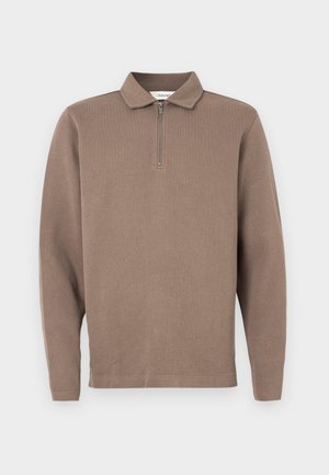 Pruun pikkade varrukatega polo särk, millel on tõmblukk kaelas, ribakujuline tekstuur ja sirge äär. Omab pikkade varrukatega lõiget ja vabamat istuvust.