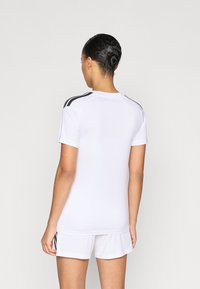 Λευκή αθλητική φανέλα με μαύρες ρίγες στους ώμους, κοντά μανίκια και ελαφρύ, αεριζόμενο ύφασμα· συνοδευόμενη από λευκό σορτς που ταιριάζει.