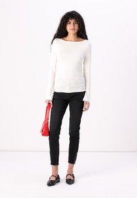Long-sleeve white top paired with black slim-fit pants, featuring zippers at the ankles. Accessories include a red handbag and black shoes with studs.
