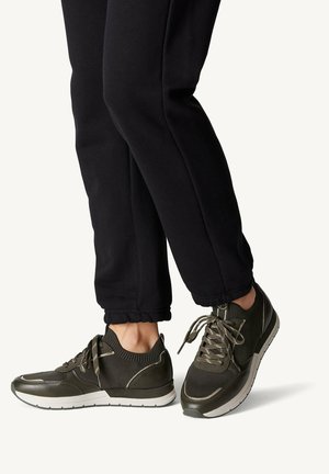 Baskets de sport vert foncé en matériau mesh et synthétique, à bout rond, à lacets et avec une semelle rembourrée, associées à un pantalon de jogging noir.