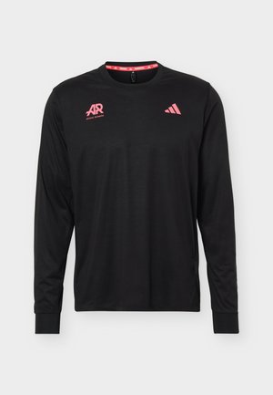 Junger Mann mit kurzen dunklen Haaren, der ein schwarzes Langarmshirt mit pinken laufbezogenen Grafiken und rote Shorts trägt, von hinten gesehen.