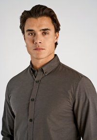 Mörkbrun skjorta med knappar framtill, klassiskt krage, subtil textur och knappstängning framtill. Skräddarsydd passform med långa ärmar.