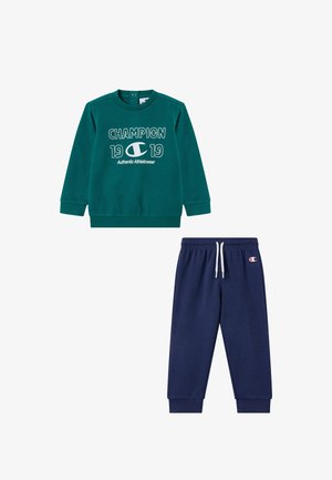 Türkisfarbenes Langarm-Champion-Sweatshirt mit Logo und dem Text "1919 Authentic Athleticwear", kombiniert mit marineblauen Sweatpants mit Kordelzugbund.