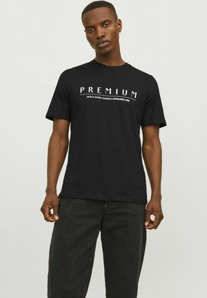 Sort bomulds t-shirt med "PREMIUM" tryk i hvid, korte ærmer, rund hals, standard pasform, båret med mørke jeans.