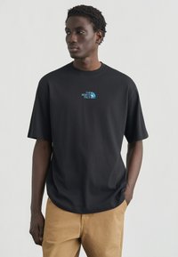 Μαύρο βαμβακερό μπλουζάκι με άνετη εφαρμογή. Διαθέτει μικρό μπλε λογότυπο "The North Face" στο στήθος. Απλός σχεδιασμός με κοντά μανίκια.