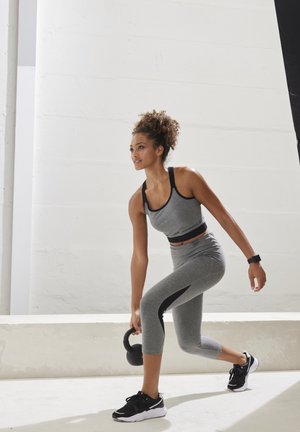 Grauer sportlicher Crop-Top und Leggings mit schwarzen Akzenten. Person hält ein schwarzes Kettlebell und trägt schwarze Laufschuhe sowie eine Uhr.
