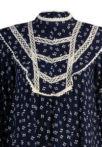 Blouse bleu marine à pois floraux blancs, col montant et bordure en dentelle blanche formant des motifs verticaux et en chevrons sur le devant.