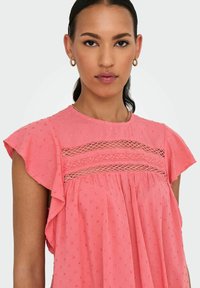 Blusa rosa con tessuto texturizzato e maniche a volant, con dettagli in pizzo al colletto e sottili motivi a pois su tutta la superficie.