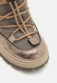 Botte de cheville beige avec un embout en bronze métallisé, un dessus en tissu texturé et une semelle en caoutchouc durable. Lacets tissés en motif croisé.