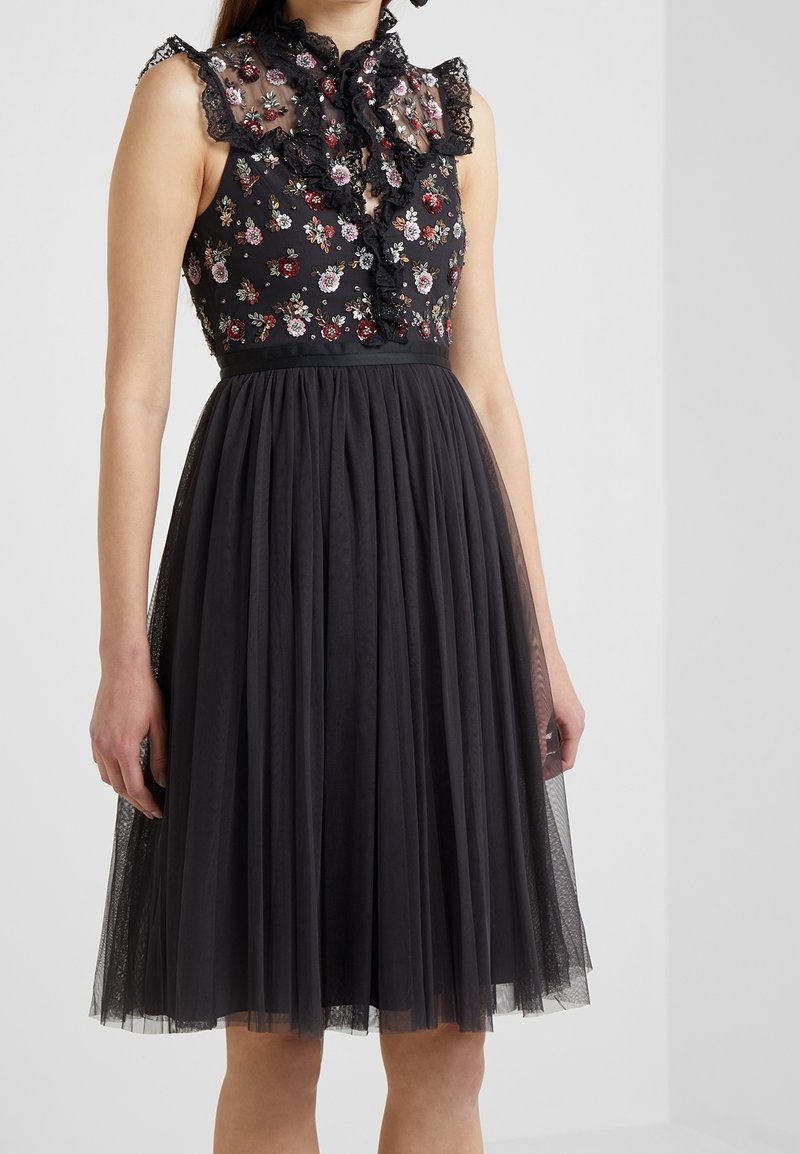 Robe noire avec broderies florales sur un bustier en dentelle transparente, col volanté et jupe en tulle, comprenant une taille ajustée et une texture superposée.