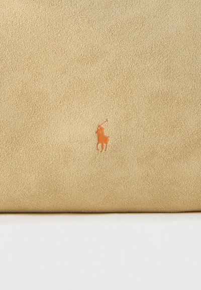 Επιφάνεια από μπεζ σουέντ δέρμα με ένα μικρό πορτοκαλί έμβλημα παίκτη πόλο πάνω σε άλογο, τοποθετημένο στο κέντρο κοντά στο κάτω μέρος.