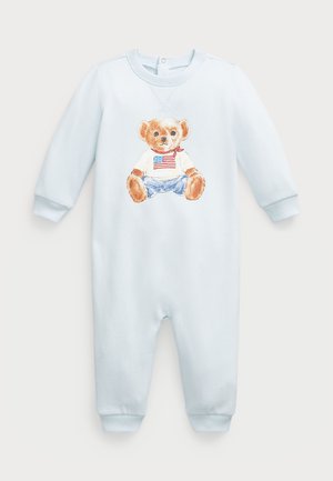 Mono de una sola pieza de color azul claro con mangas largas, que presenta una ilustración de un oso con camiseta y jeans. El material parece suave y texturizado.