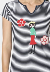 Top de algodón rayado en azul marino y blanco con escote en V, que presenta un personaje bordado en verde y rojo con apliques de flores.